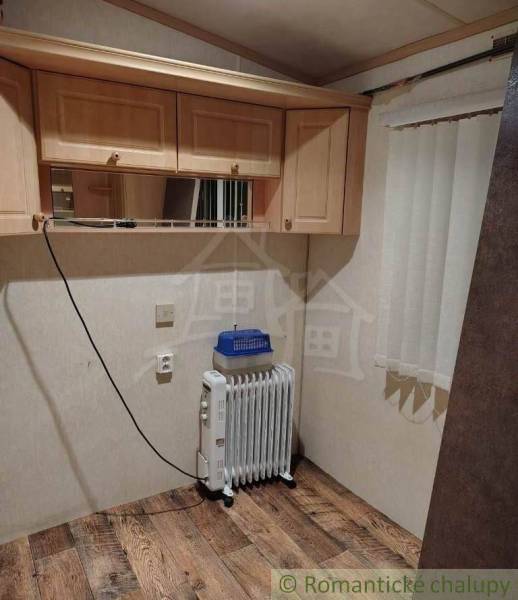 A room in a family house with a radiator, shelves, light-colored cabinets, wooden floor, and curtains.