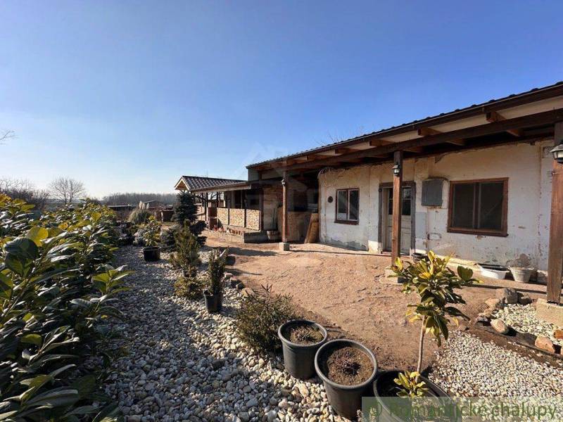 Family house with a veranda, gravel path, flower pots, and a landscaped garden for sale.