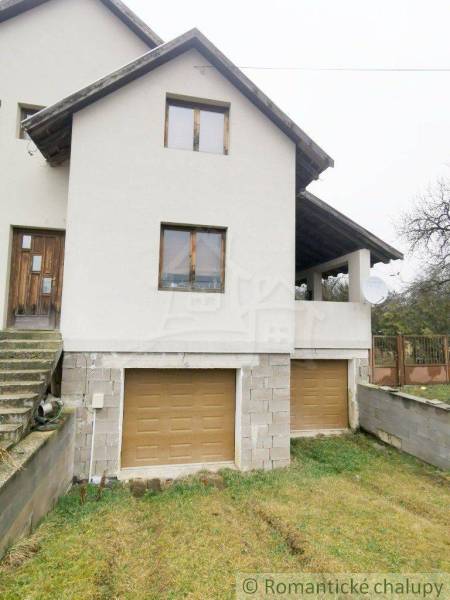 A family house with a white facade, wooden windows, and a double garage entrance.