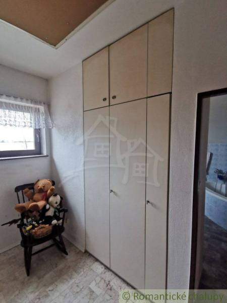 A room in a family house with a white wardrobe, toys on a chair, and a window with a curtain.