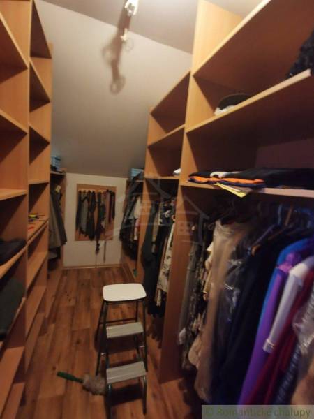 Wardrobe with clothes and a ladder in a family house. Wooden shelves and hangers.