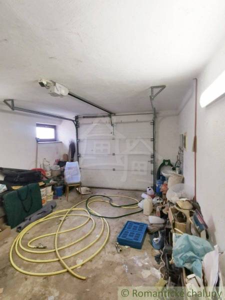 A garage with stored items, a hose, and a family house in the background.