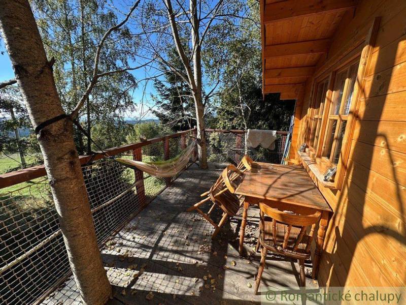 Wooden terrace with a swing and a table, surrounded by nature near a family house.