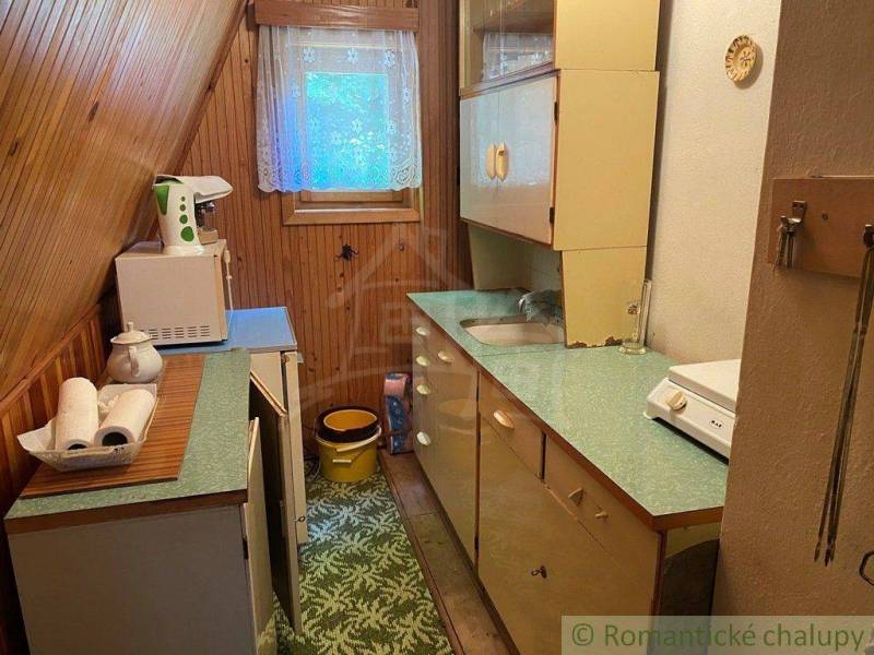 A country kitchen in the attic with wooden paneling, a window, kitchen cabinets, and appliances.