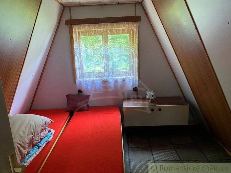 Attic room with a bed, wooden walls, and a window in a family house.