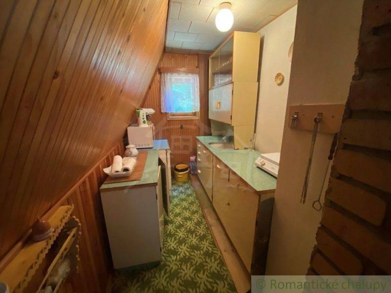 Narrow wooden kitchen with a refrigerator, cabinets, and a window in a family house.
