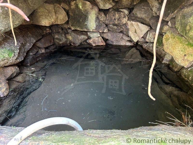 A stone well with water surrounded by stones, a natural feature near a family house.