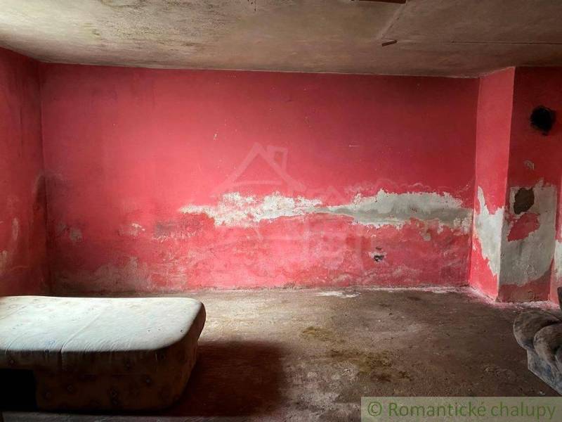 A shabby room with a red wall, a worn-out mattress; visible signs of dampness.