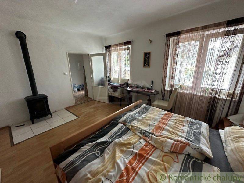 A room in a family house with a tiled stove, a bed, curtains, and large windows.