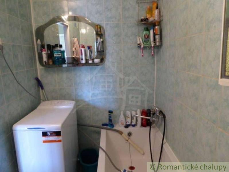 A bathroom with green tiles, a washing machine, a mirror, and a lot of cosmetics. Family house.