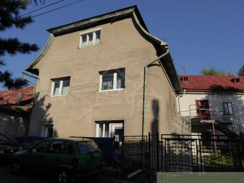 A two-story family house with a metal roof, an external staircase, and a parked green car.