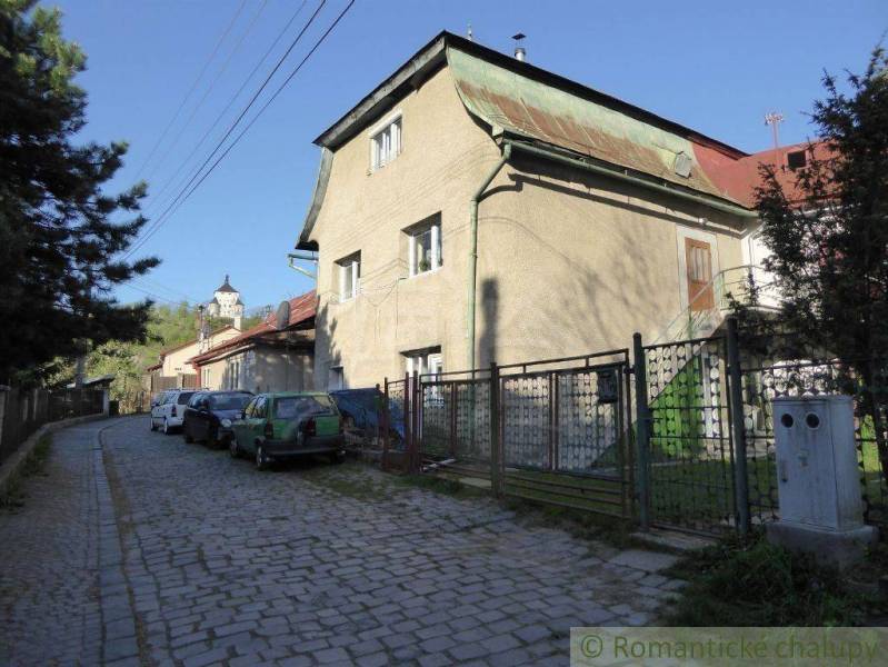 A family house with a metal roof by the road, surrounded by cars and a fence.