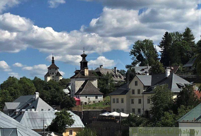 A historic town with church towers, green trees, and a blue sky with clouds.