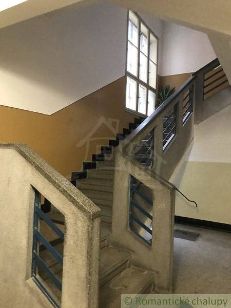A staircase in an apartment building with windows and a railing, leading to apartment doors.