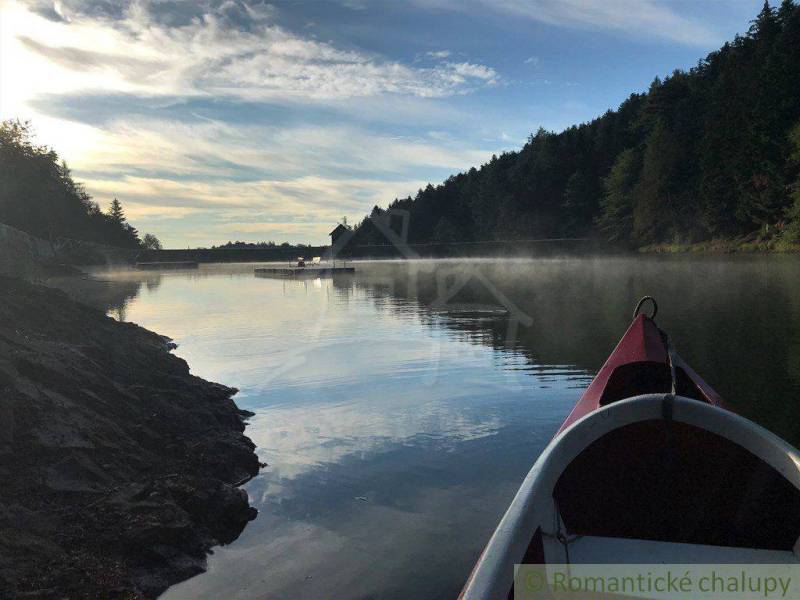 A boat on a calm lake surrounded by forest, the setting sun creates a reflection on the water.