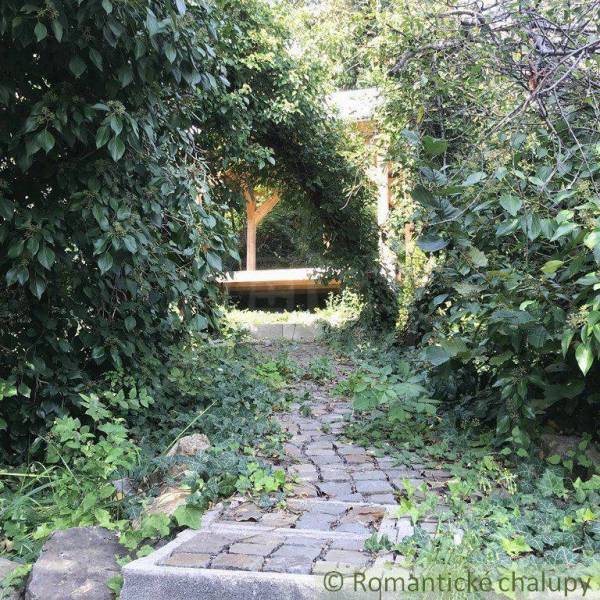 A romantic garden with unique properties, a stone path leads to a wooden gazebo surrounded by greenery.
