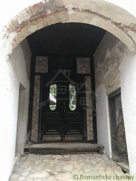 A stone pavement leads to historic wooden doors, surrounded by a brick arch.