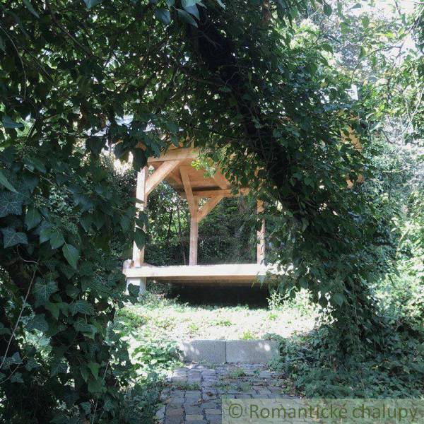 A comfortable wooden gazebo in nature, surrounded by lush greenery and peculiar properties.