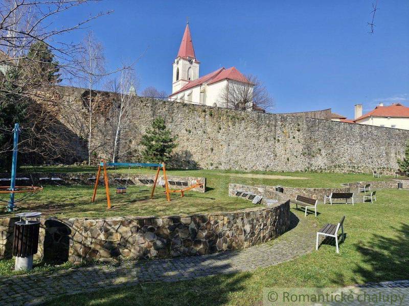 A children's playground with swings near a historic church and a stone wall in the park.