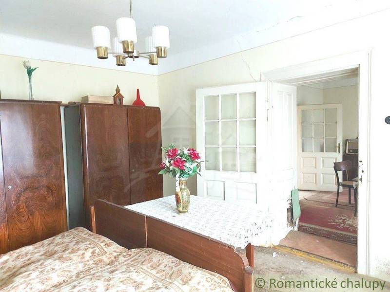 A room with a wooden wardrobe, a bed, a table decorated with flowers; a typical cottage.