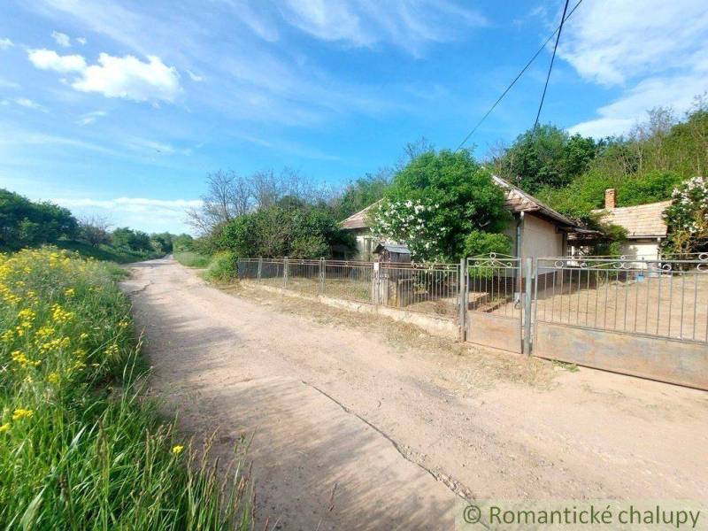 The path leads past a romantic cottage surrounded by nature and shrubs, under a blue sky.