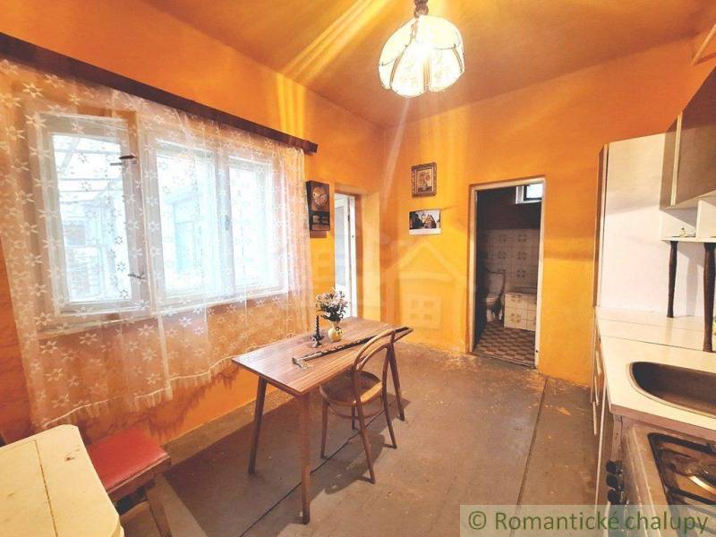 A kitchen in a family house, curtains, a table, chairs, a door leading to the toilet.