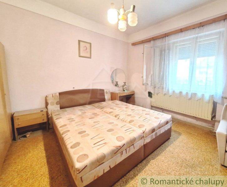 A bedroom with a double bed in a family house, decorated with simple furniture and curtains.