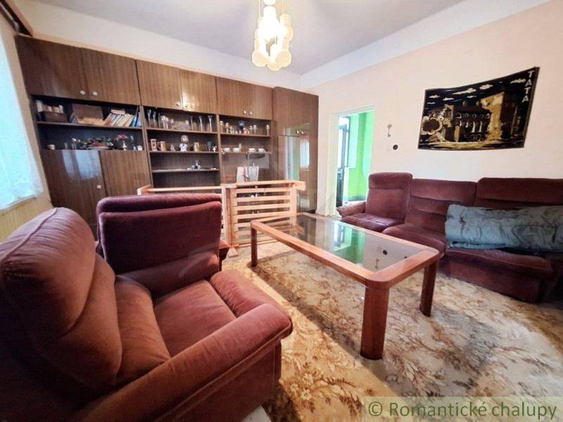 A living room in a family house with rustic furniture, red armchairs, and a wooden bookshelf.