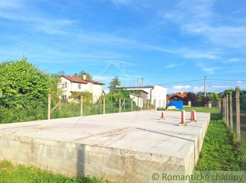 A foundation slab on a construction site surrounded by a garden and plants, blue sky.