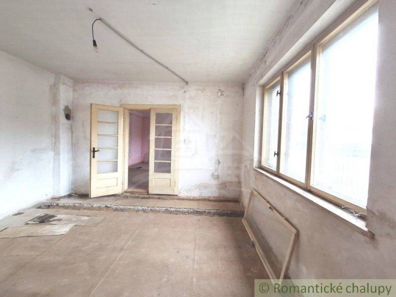 Interior of a cabin for renovation with large windows, white walls, and double doors.