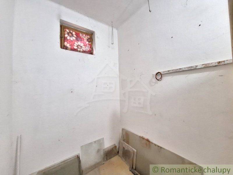 A small room in a cottage with white walls, a window with a patterned curtain.