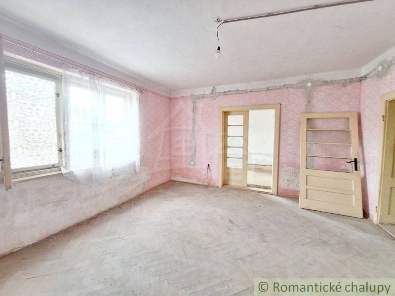 A room in an older cottage with pink walls, wooden floors, and large windows.
