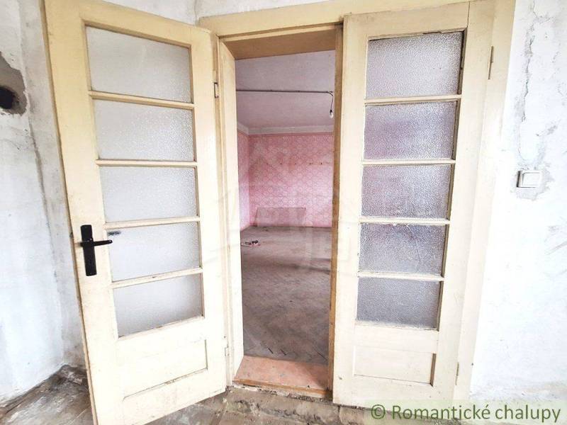 Worn double doors leading to a room with pink walls in a cottage.