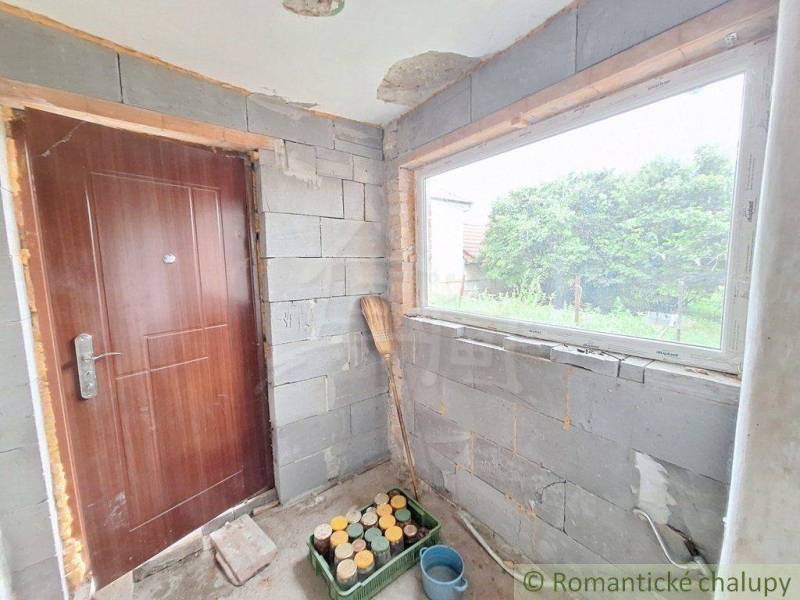An interior with an unplastered wall, door, window, and tools, suitable for a cottage and gardeners.