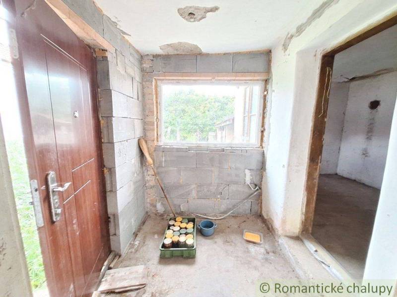 A cottage under reconstruction with wooden doors, a window without glazing, and an entrance to the room.