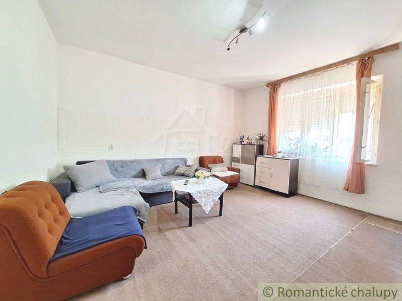 Living room in a family house with an upholstered sofa, a table, and windows with curtains.