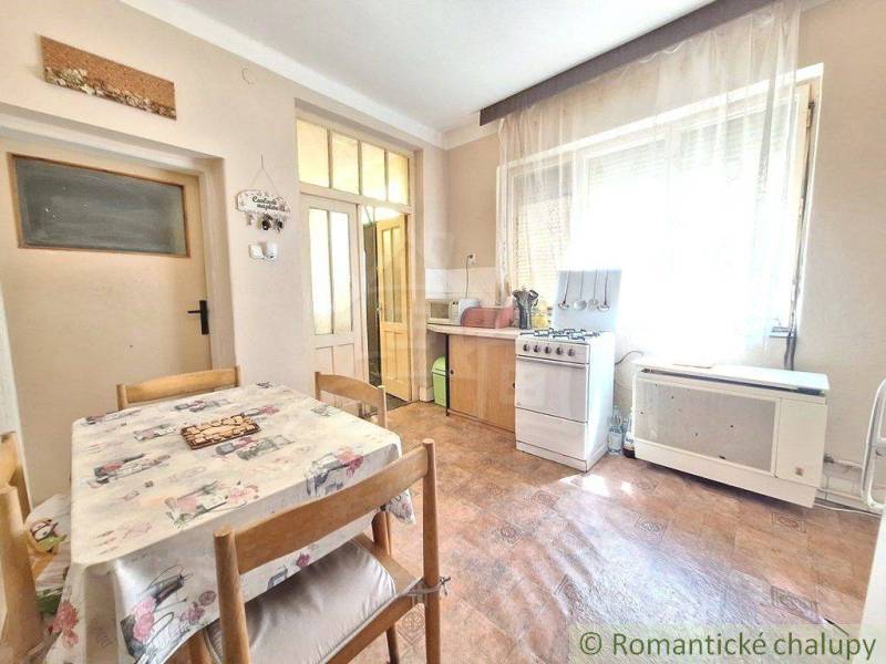 Dining room and kitchen in a family house with a table, chairs, a gas stove, and large windows.
