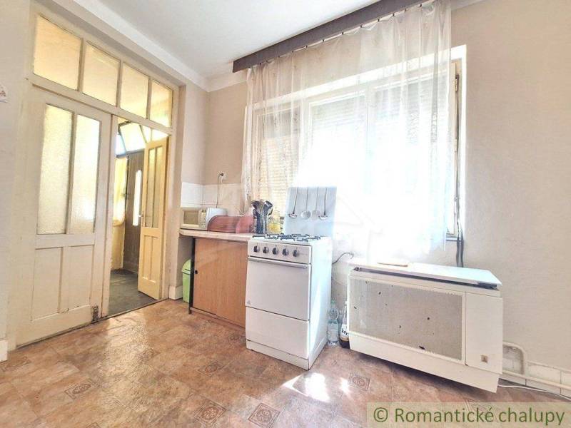 A kitchen in a family house with a gas stove, window, door, curtain.
