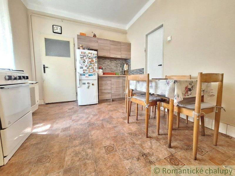 The kitchen in the family house contains a stove, a refrigerator, a dining table, and wooden chairs.