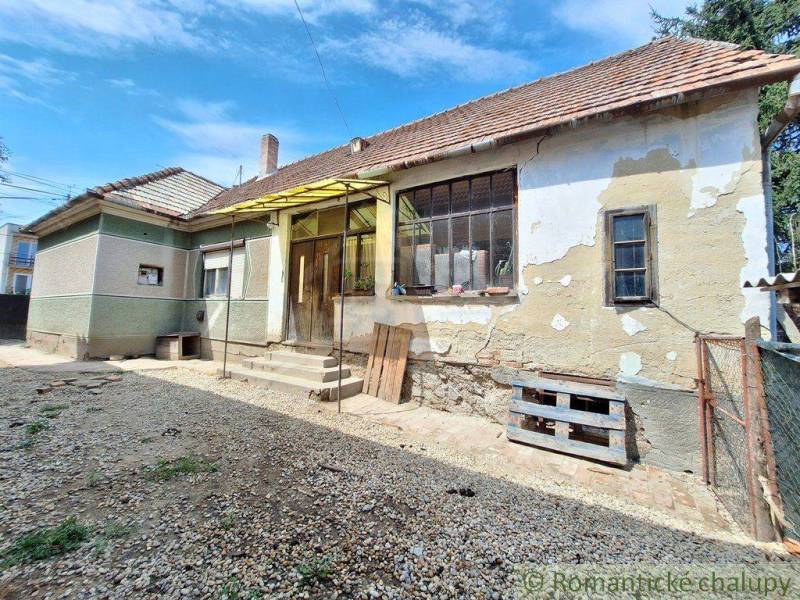 A family house with plaster needs renovation, a stone-covered yard, and stairs.