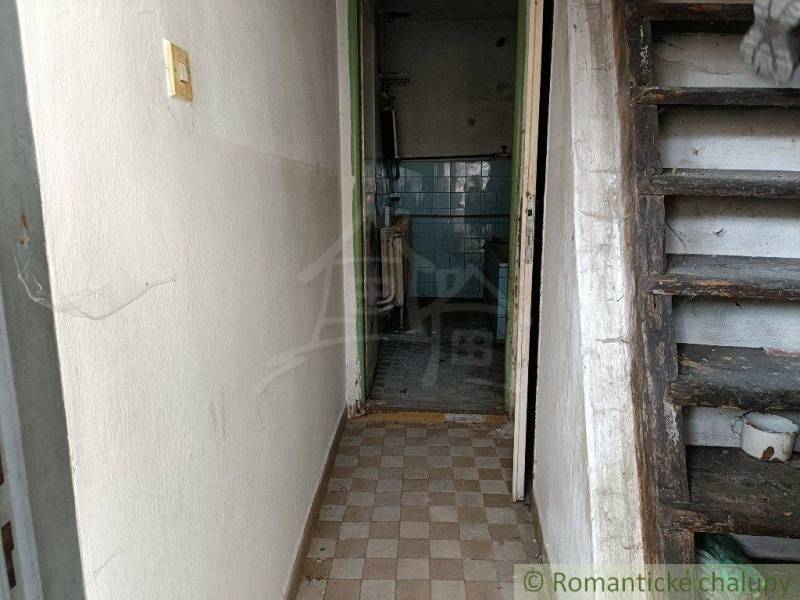 Entrance hallway with wooden stairs and tiled walls in a neglected family house.