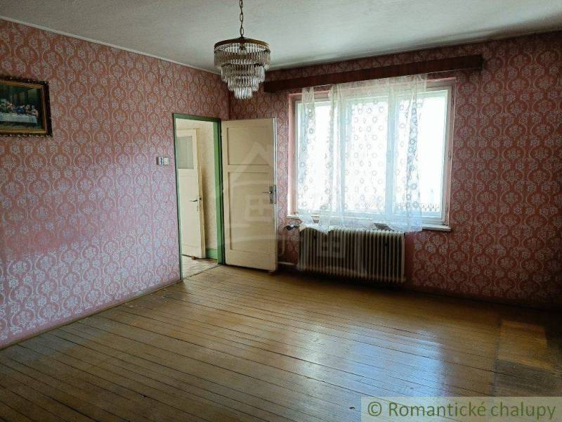 A room with older patterned wallpaper, wooden flooring, and a chandelier.