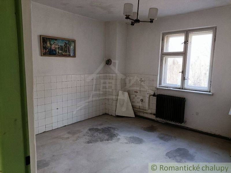 An empty room with white tiles, a radiator, and a painting in an older family house.