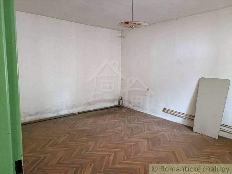 A room with a damaged floor, white walls, and an old light fixture, family house.
