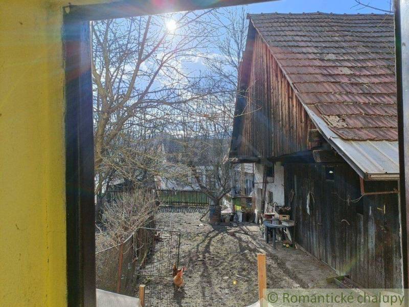 A view from the window of a courtyard with a chicken and a wooden shelter near a family house.