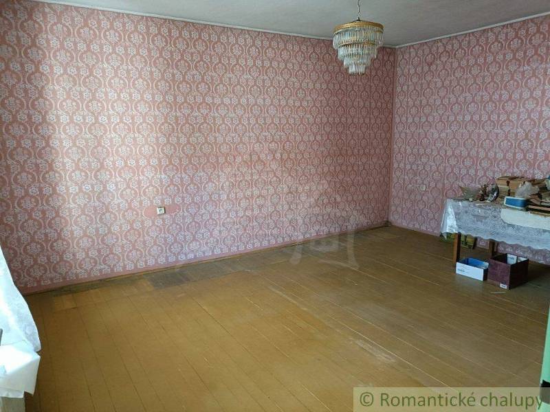 A room with patterned wallpaper, a simple light fixture, wooden flooring, and a table in a family house.