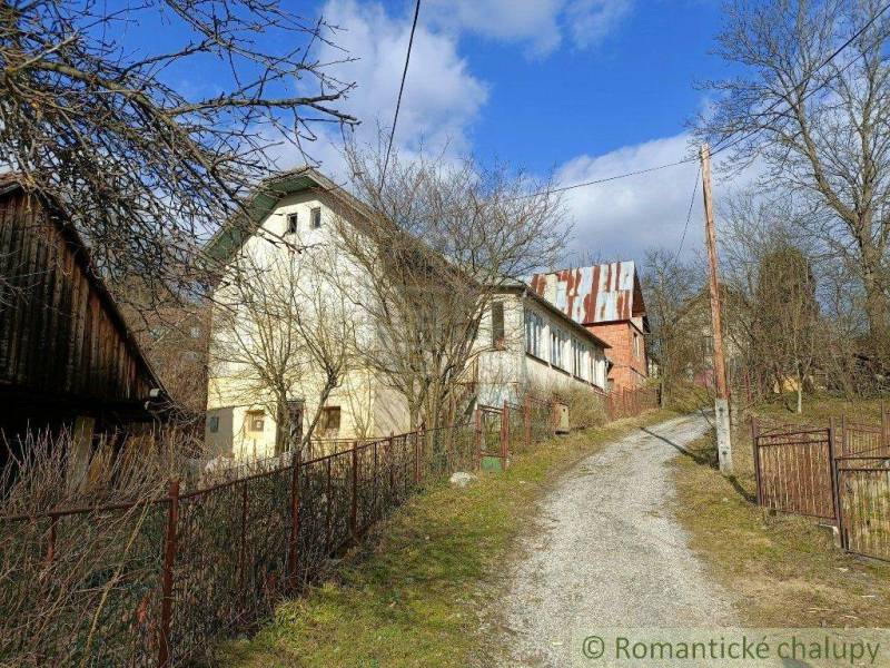 I see an older family house surrounded by nature, a driveway, and a blue sky.