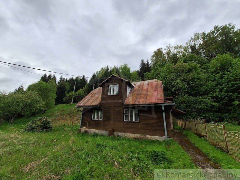 A cottage in Veľké Rovné surrounded by greenery, bordered by an old fence and trees.