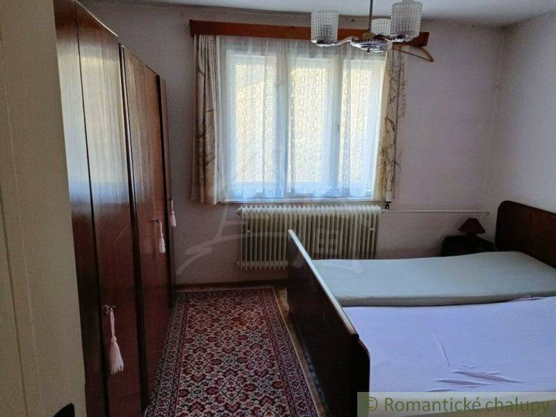 A bedroom in a cottage with a wooden wardrobe, carpet, and two beds under the window.