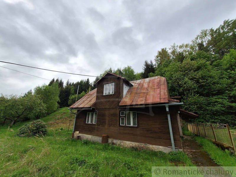 A wooden cottage in Veľké Rovné surrounded by greenery and a slightly cloudy sky.